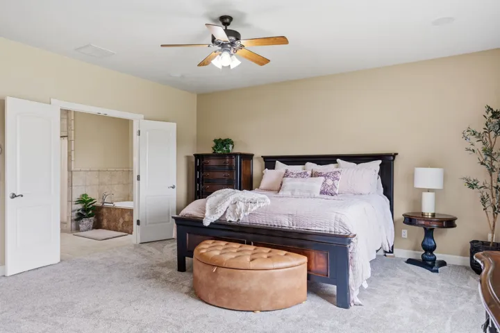 Spacious bedroom with plush carpeting, ceiling fan, and French doors opening to a tiled bathroom with a built-in tub