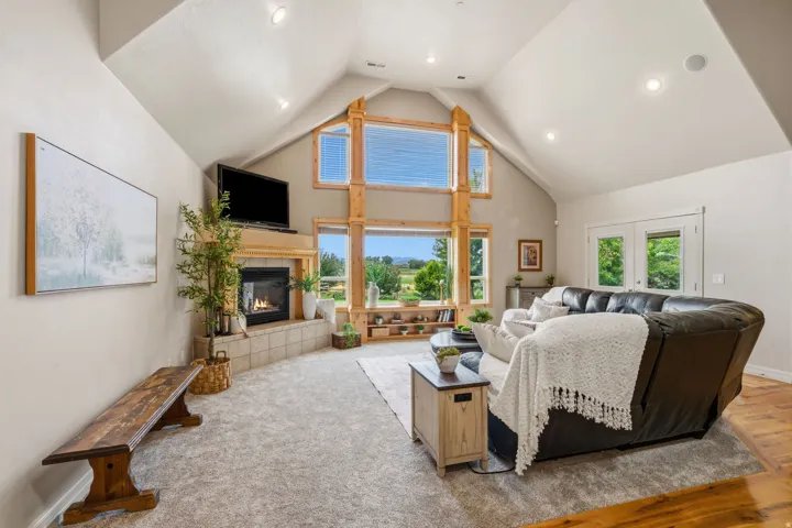 Vaulted ceiling with recessed lighting, floor-to-ceiling windows with wood trim, gas fireplace with tile surround, wood-finish flooring, and French doors