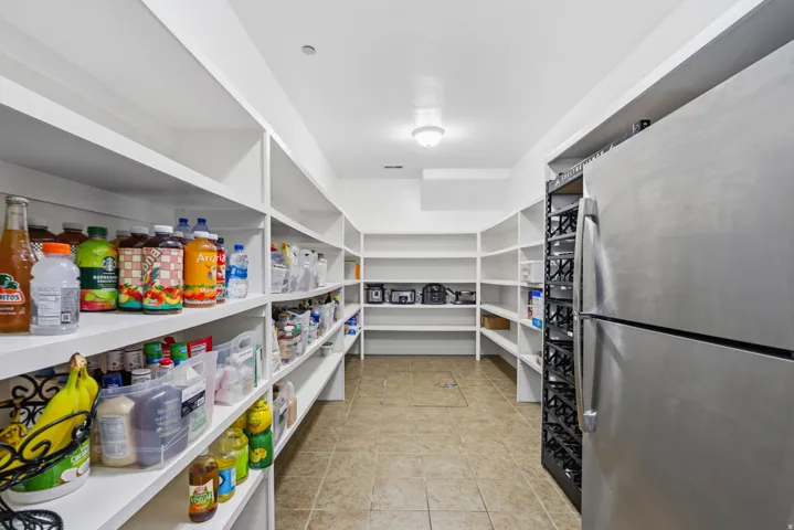 Spacious pantry with extensive built-in shelving, tile flooring, and a stainless steel refrigerator