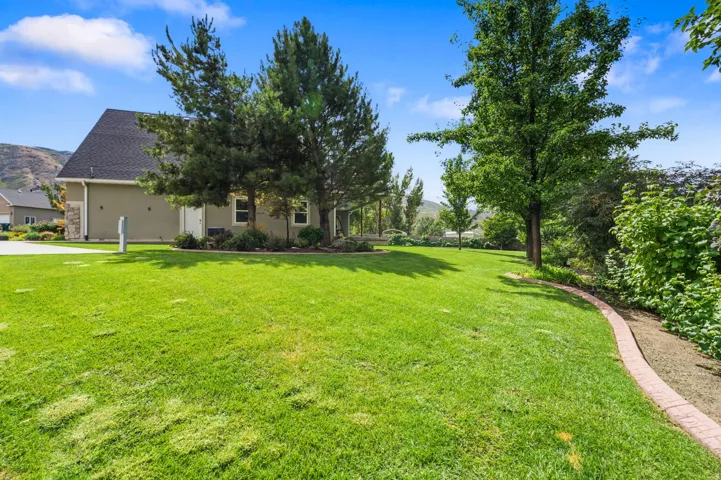 Expansive lawn with mature trees, a defined garden bed with brick edging, and a stucco exterior with stone accents