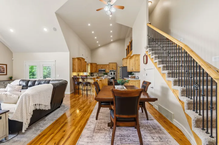Vaulted ceilings with recessed lighting, wood-finish flooring, wood cabinetry, carpeted staircase with wrought iron balusters, and double glass-paneled doors