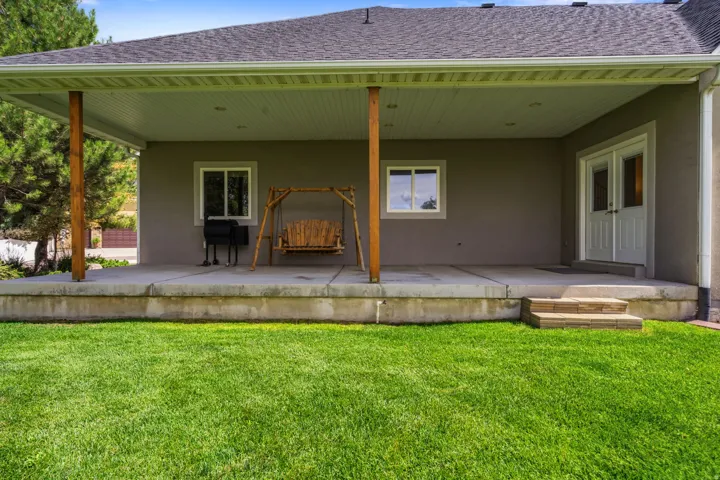 Covered concrete patio with wood support columns, recessed lighting, and dual French doors