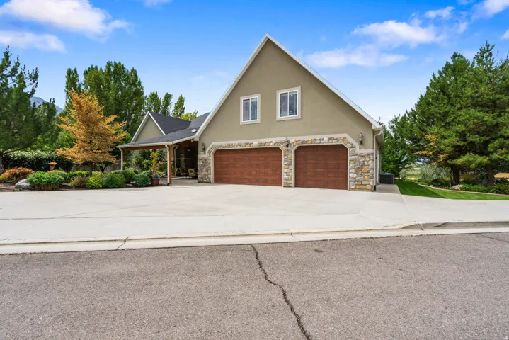 Stucco exterior with stone accents, two-car garage with wood-finish doors, covered entry, and mature landscaping