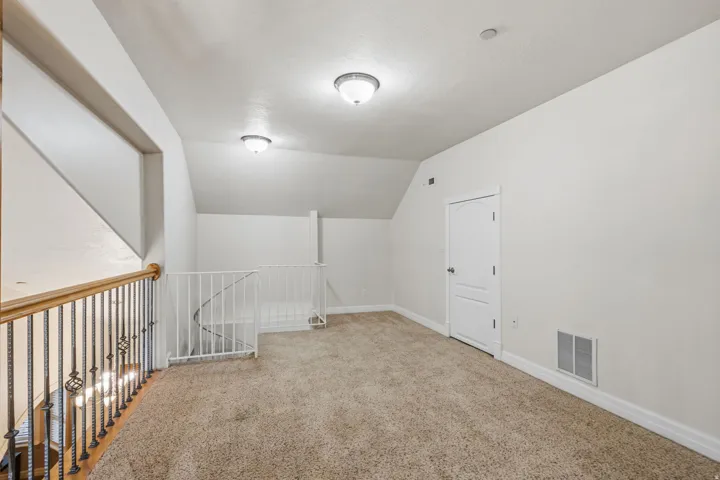 Carpeted loft space featuring sloped ceilings, white paneled door, and iron baluster railing with wood-finish handrail