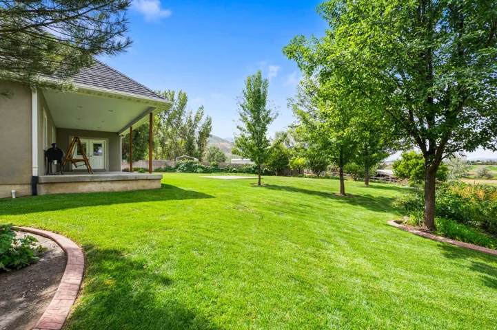 Expansive lawn with mature trees and a covered patio featuring wood support columns