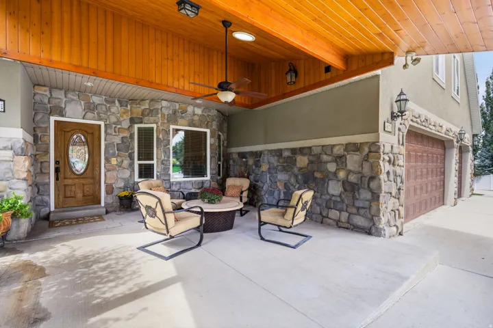 Covered front patio featuring a wood-panel ceiling, stone veneer accents, and recessed lighting