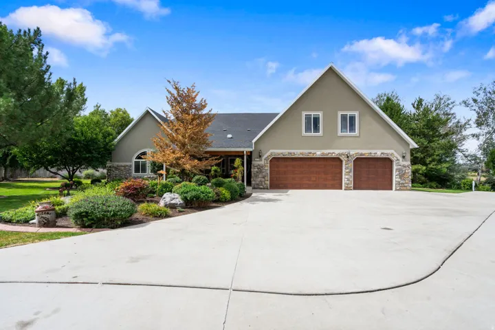 Stucco exterior with stone accents, two-car garage with wood-finish doors, arched window, mature landscaping, and an expansive concrete driveway