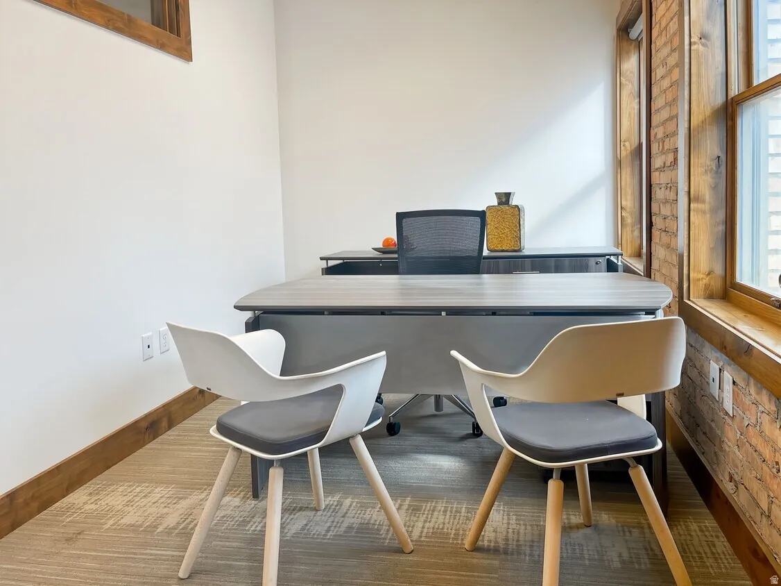 Exposed brick wall, wood-finish window trim, light-toned carpeting, and wood-finish baseboard
