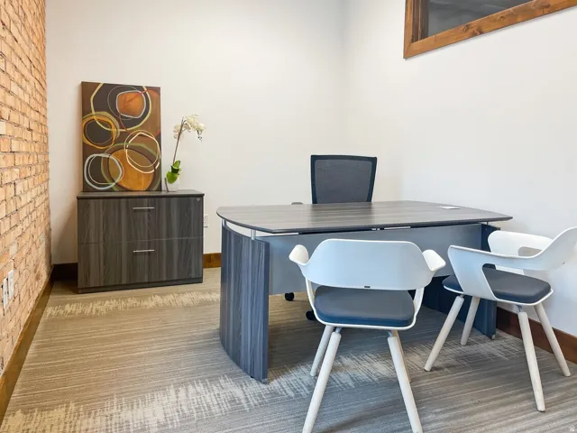 Exposed brick accent wall, neutral tone carpeting, white painted walls, and wood trim detailing
