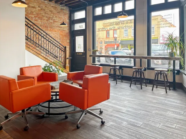 Exposed brick wall, wood-finish flooring, black window framing, built-in wooden bar, and industrial pendant lighting