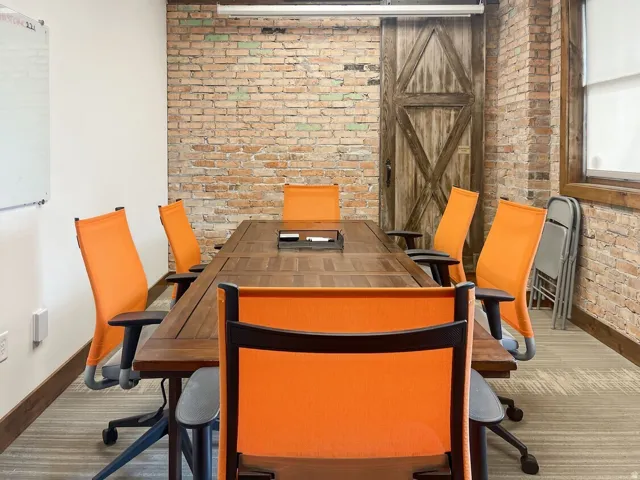 Exposed brick wall, barn door, wood-finish conference table, white board, and light-colored carpet