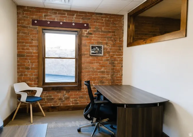 Exposed brick wall with a single window featuring a wood-finish frame, wood-finish flooring, and a drop ceiling