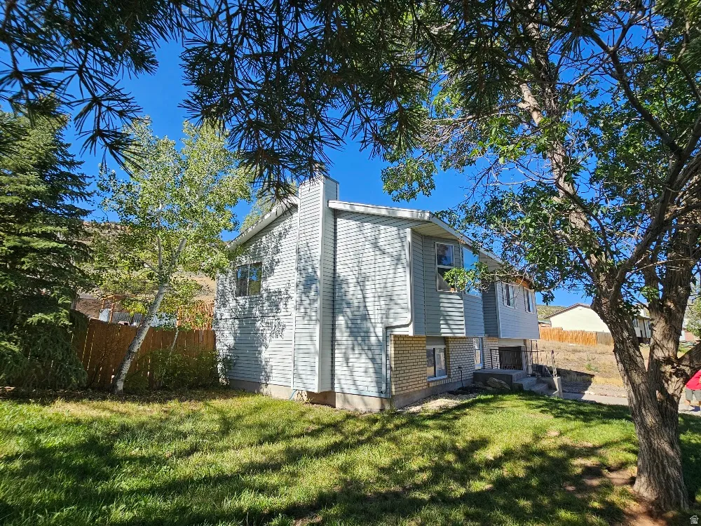 Expansive green lawn, mature trees, wood privacy fence, siding exterior, and a visible chimney structure