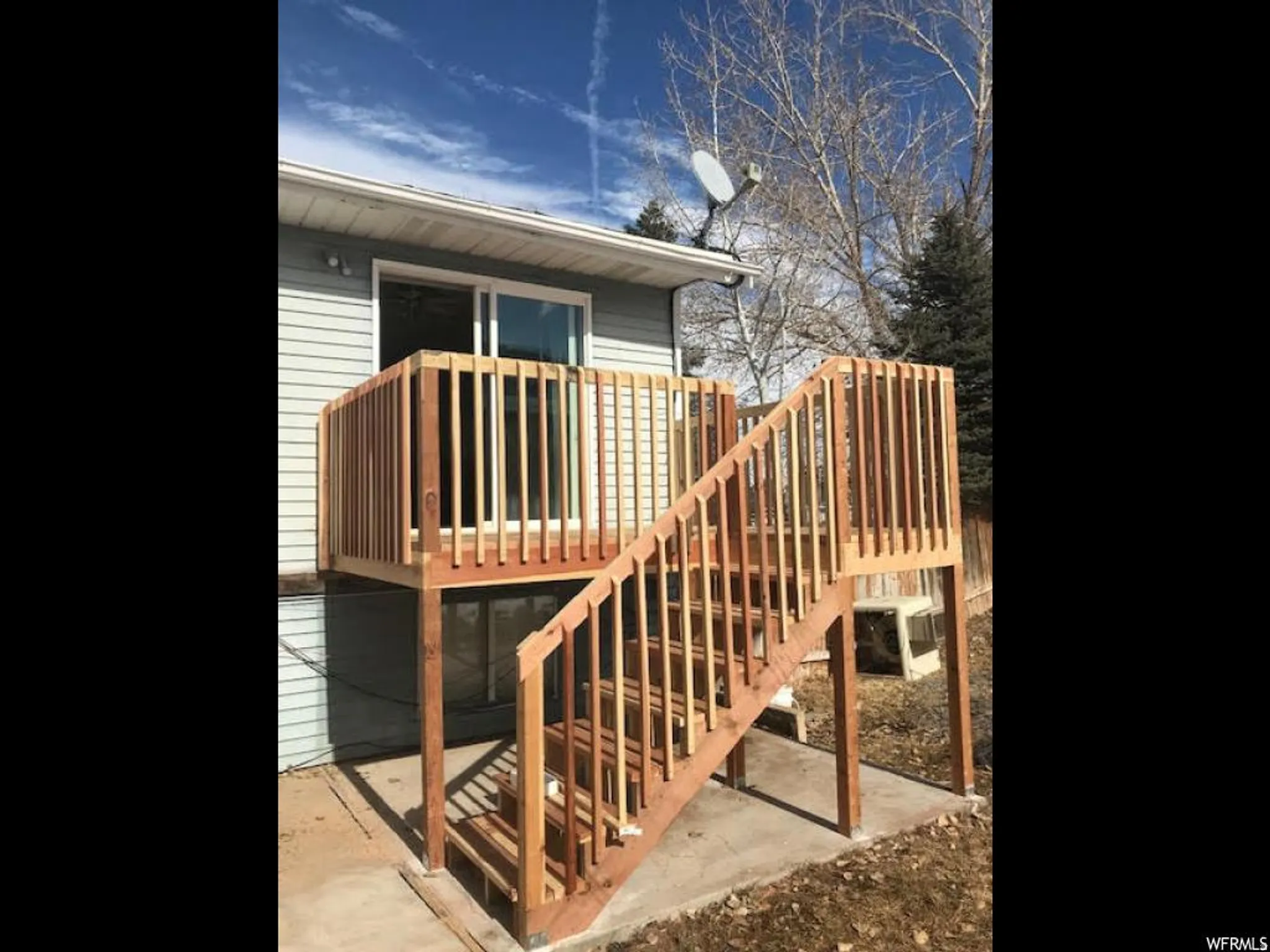 Newly constructed wood deck with railings, concrete pad, and siding exterior