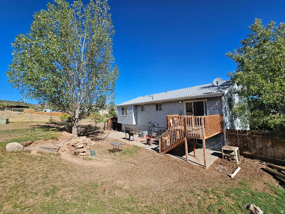 Rear exterior featuring a wood deck, sliding glass door, and a mature tree