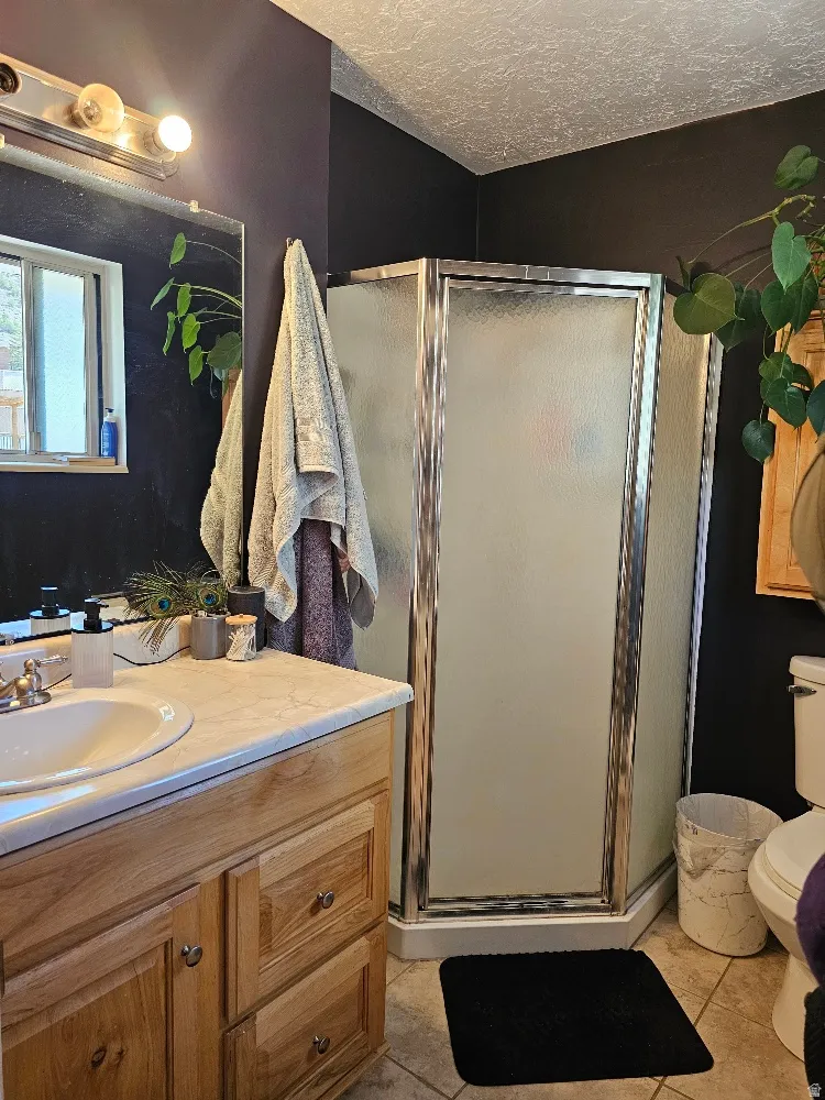 Bathroom featuring a wood-finish vanity with an integrated sink, a corner shower with a framed frosted glass enclosure, and tiled flooring