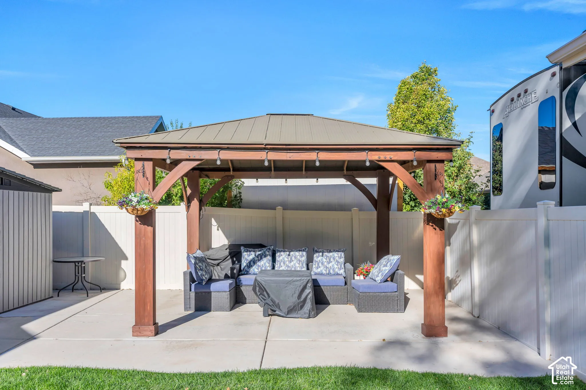 Backyard featuring a wooden pergola with a metal roof, concrete patio, white privacy fencing, and a utility shed