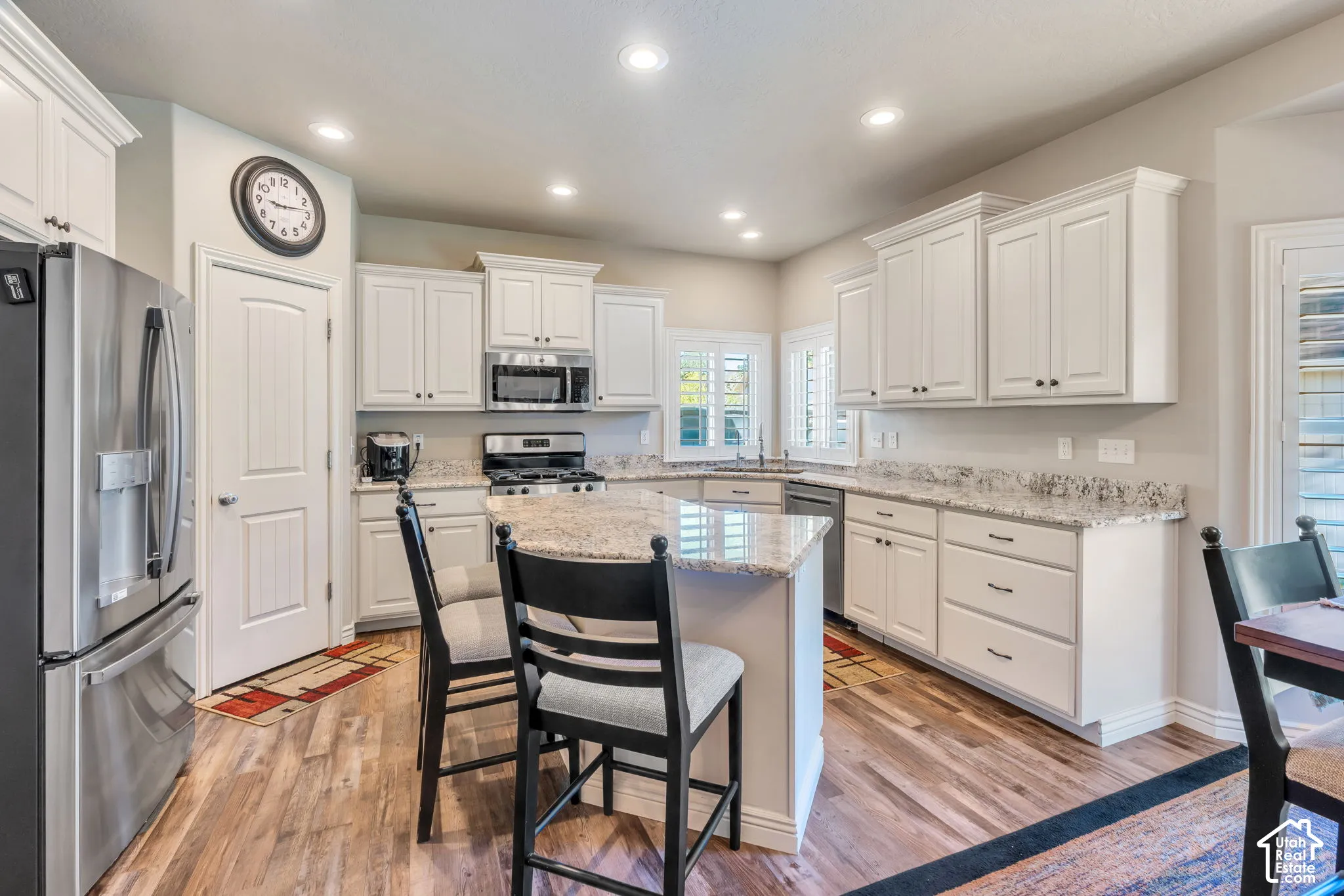 Kitchen with white cabinetry, stainless steel appliances, recessed lighting, LVP flooring, and a kitchen island with granite countertop