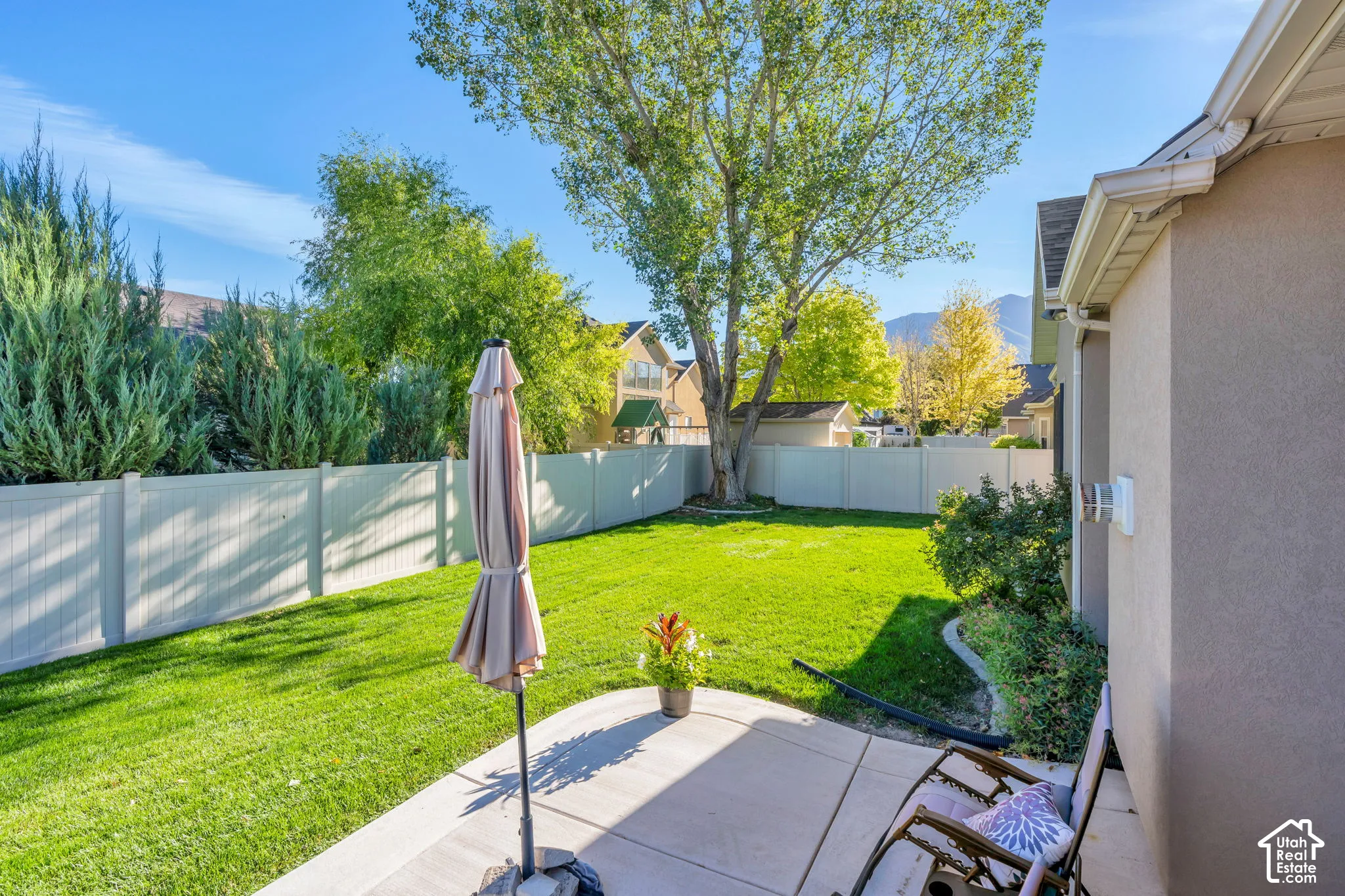 Expansive backyard featuring a concrete patio, a manicured lawn, a privacy fence, and mature trees