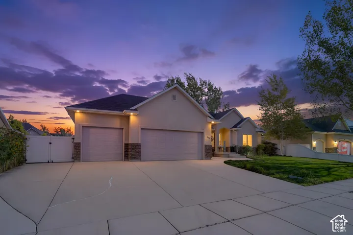 Stucco exterior with stone accents, two-car garage, expansive concrete driveway, and covered front entry