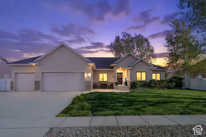 Stucco exterior with stone accents, two-car garage, covered entry, front lawn, and paved driveway