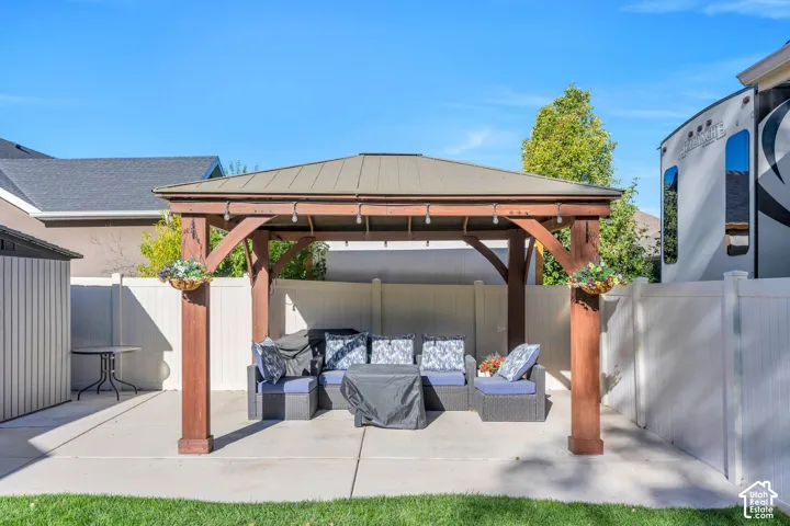 Backyard featuring a wooden pergola with a metal roof, concrete patio, white privacy fencing, and a utility shed