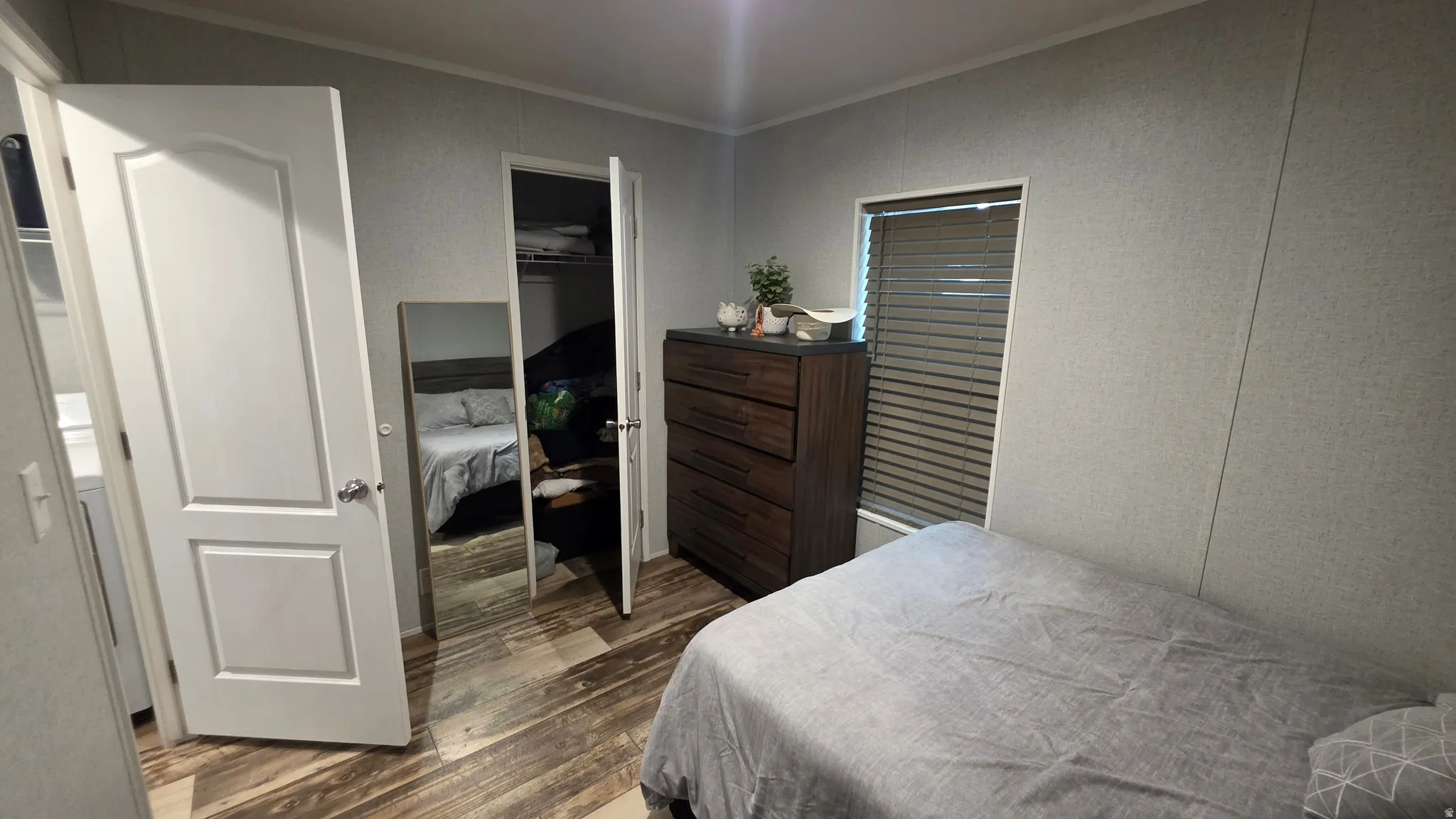 Wood-finish flooring, white paneled door, window with blinds, and built-in closet