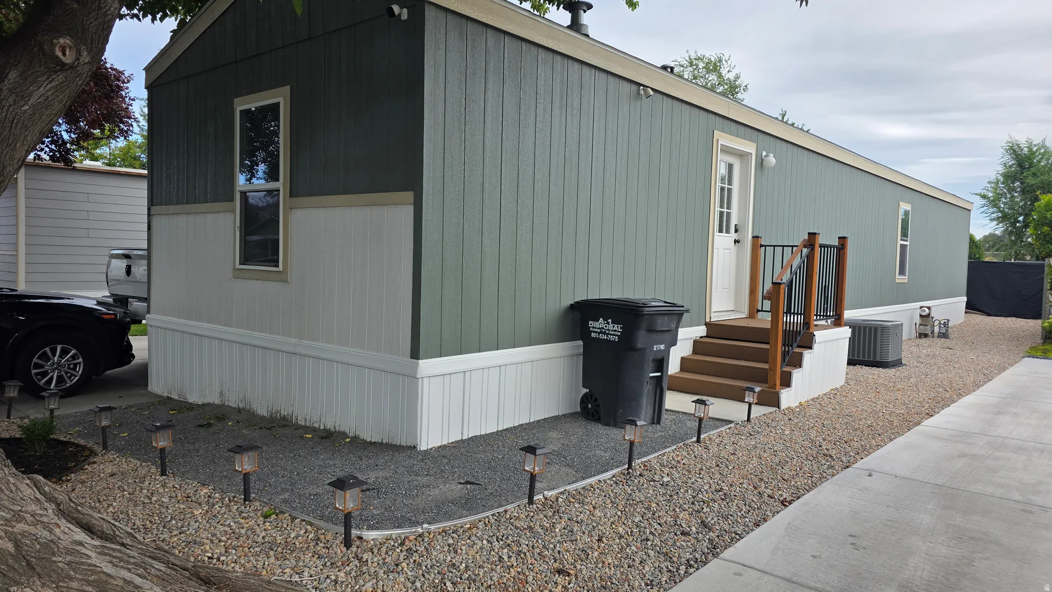 Exterior featuring two-tone vertical siding, wood-finish steps with dark metal railing, and gravel landscaping