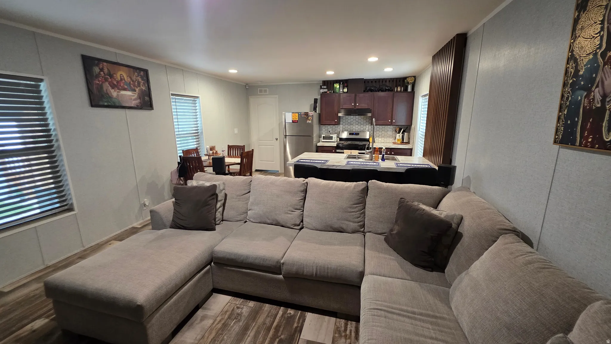 Open-concept living area with wood-finish flooring, recessed lighting, and a kitchen featuring dark wood cabinetry, stainless steel appliances, and a tiled backsplash