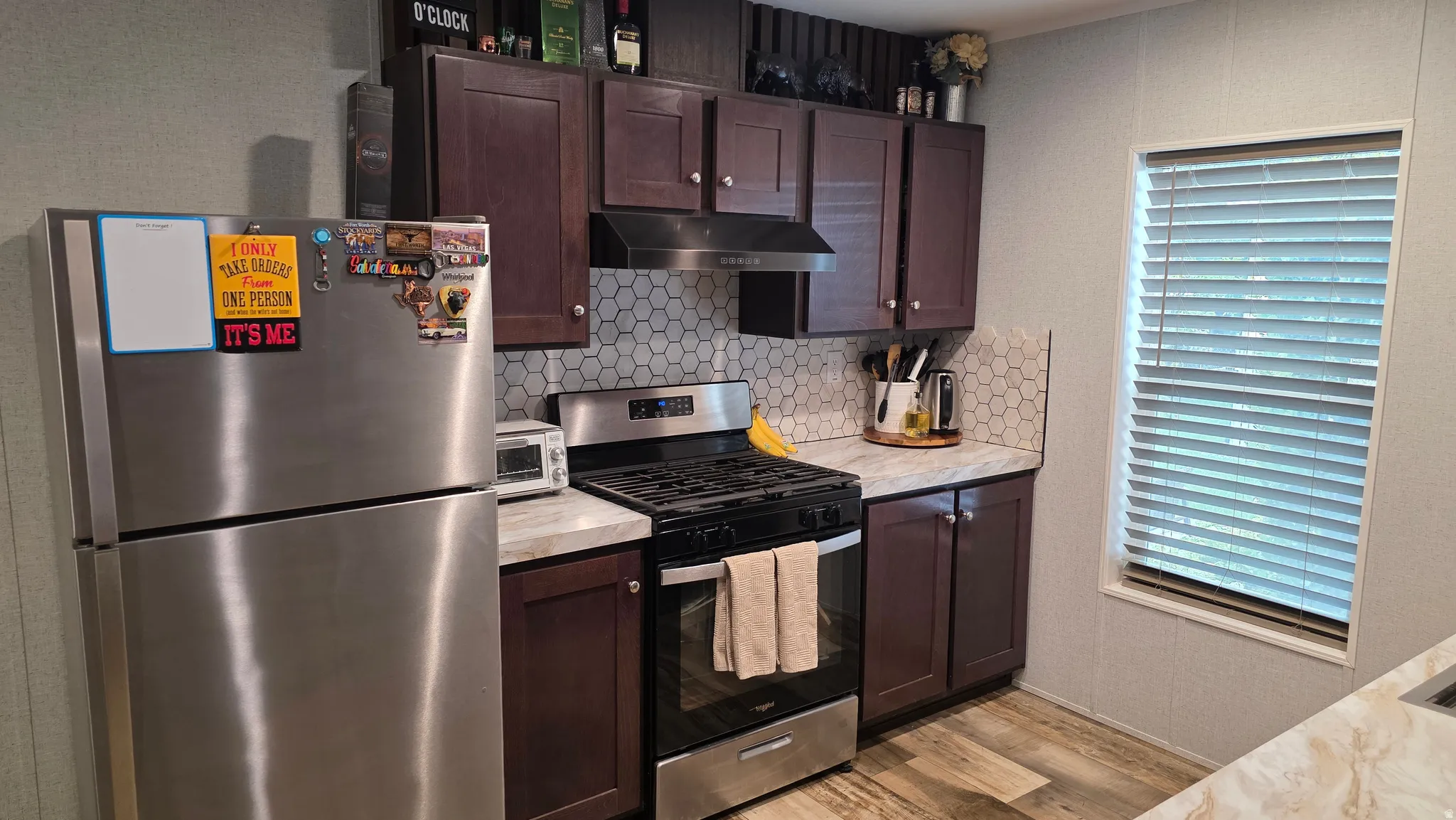 Kitchen featuring wood-finish cabinetry, stainless steel appliances, honeycomb tile backsplash, and light-toned countertops