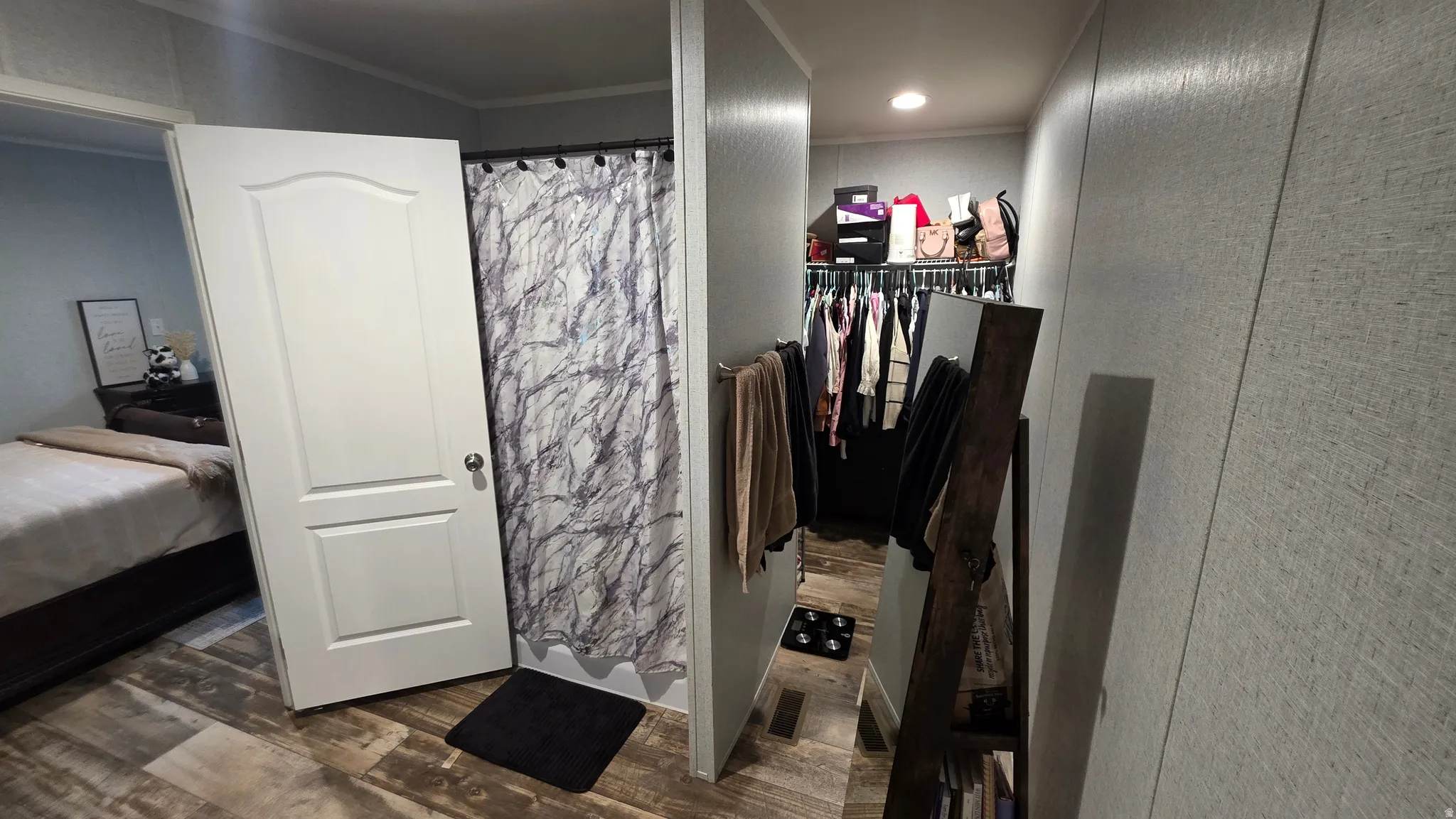 Wood-finish flooring throughout, shower stall with curtain, and a walk-in closet with built-in shelving