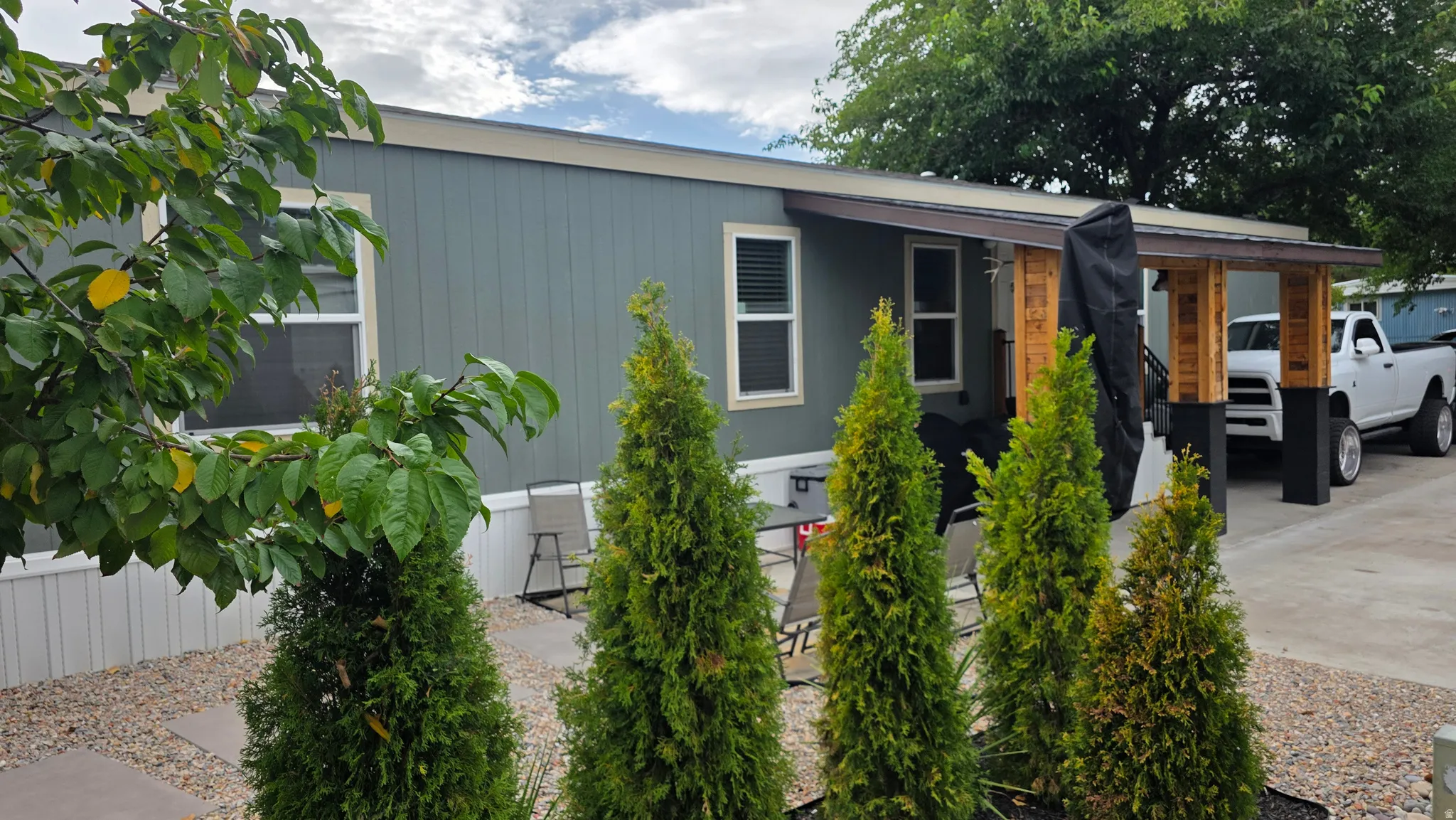 Siding exterior with multiple windows, covered porch with wood-wrapped supports, and landscaping with mature plantings