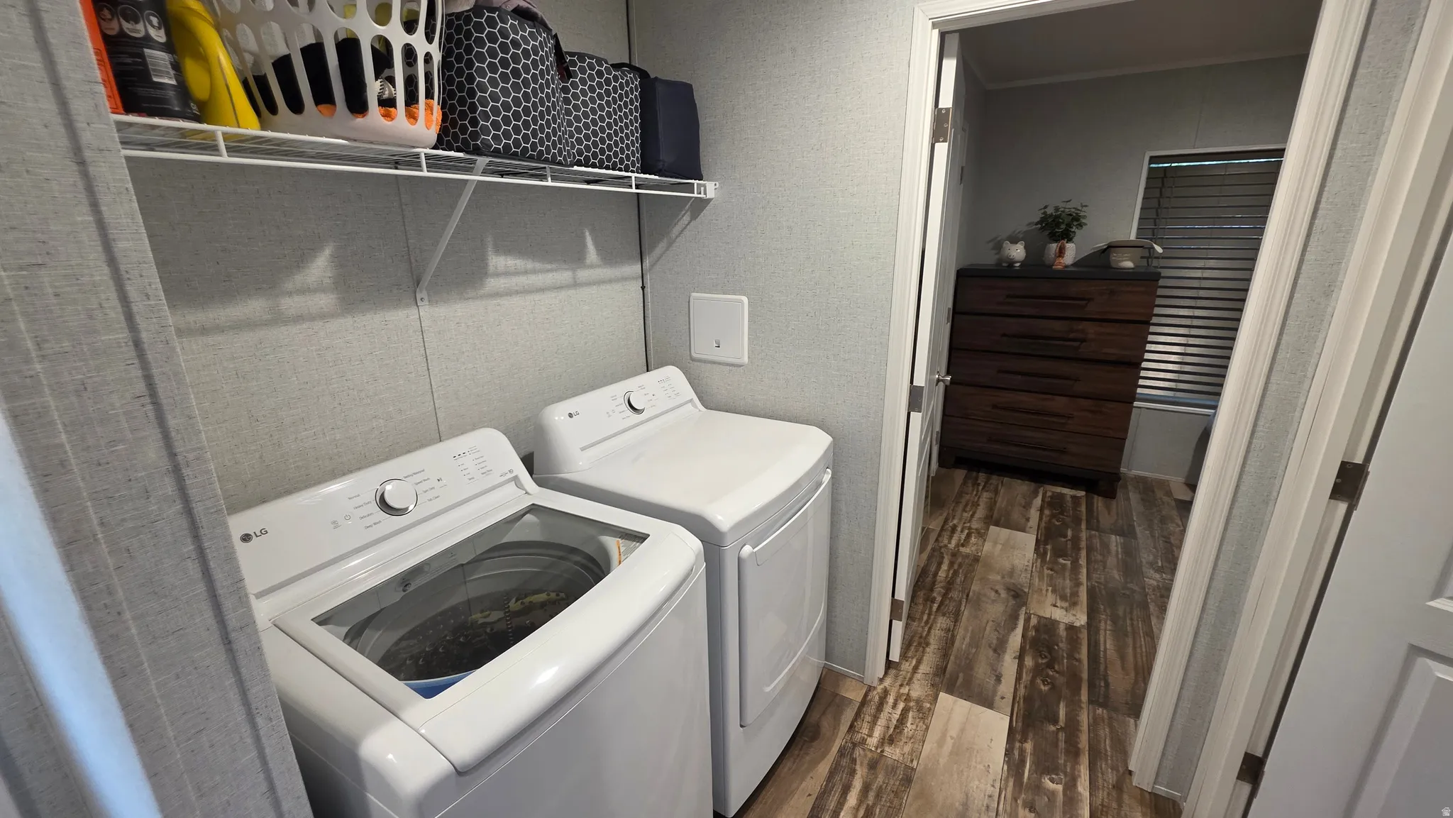 Laundry area featuring a wire shelving unit, wood-finish flooring, and light-toned wall covering