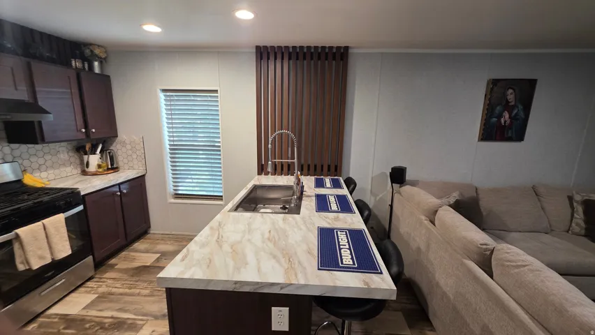 Kitchen featuring a stainless steel range with a ventilation hood, hexagonal tile backsplash, wood-finish flooring, and a central island with an integrated sink