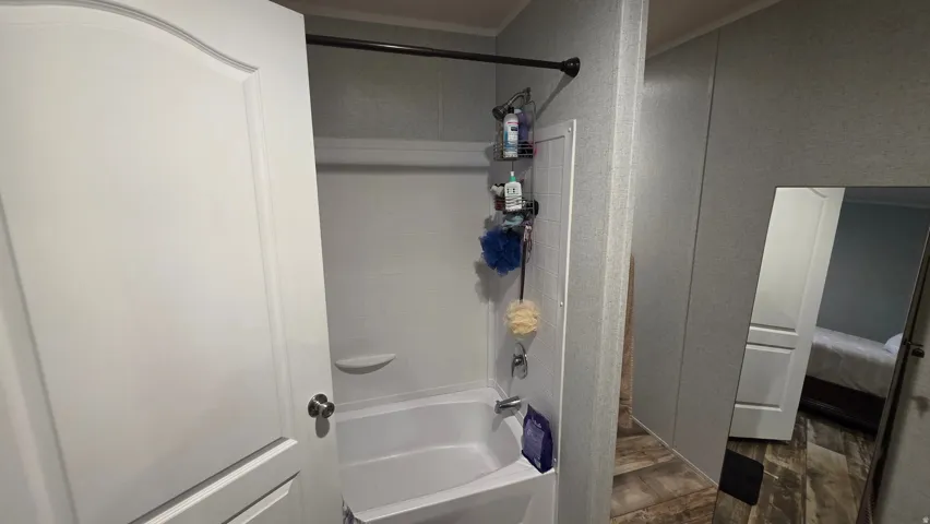 Bathtub and shower combination with a shower head and rod, paneling walls, and wood-finish flooring