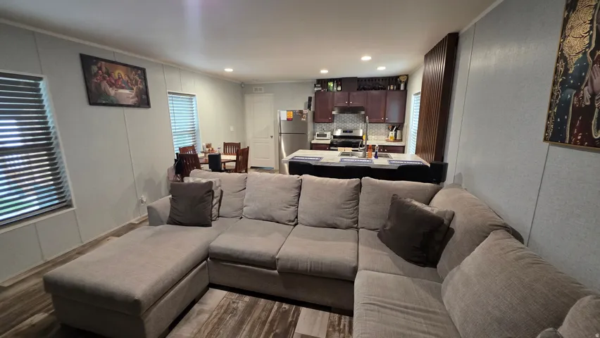 Open-concept living area with wood-finish flooring, recessed lighting, and a kitchen featuring dark wood cabinetry, stainless steel appliances, and a tiled backsplash
