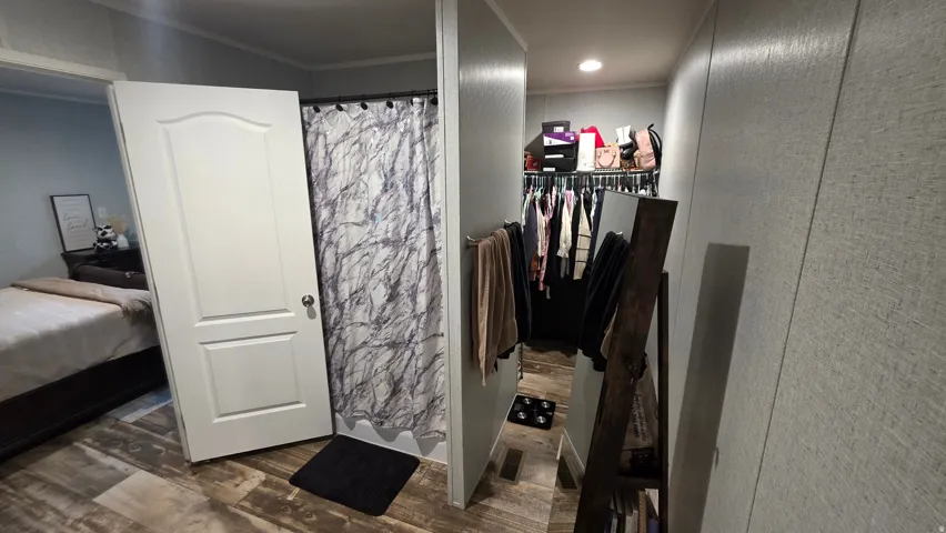 Wood-finish flooring throughout, shower stall with curtain, and a walk-in closet with built-in shelving