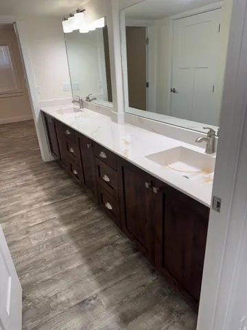 Dual basin vanity with rich, cabinetry, white countertops, dual mirrors, and brushed nickel fixtures