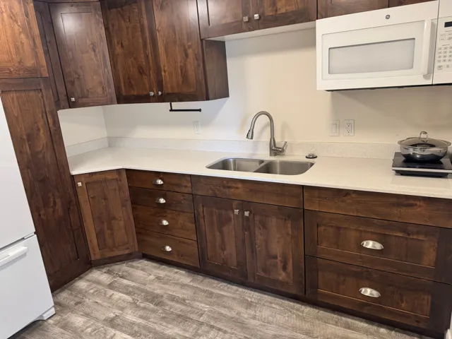 White countertops with an undermount double basin sink, dark-finish cabinetry, Vinyl flooring, and a white over-the-range microwave
