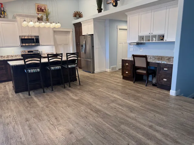 Vinyl flooring throughout, kitchen island with seating, built-in desk area, stainless steel refrigerator, and built-in microwave