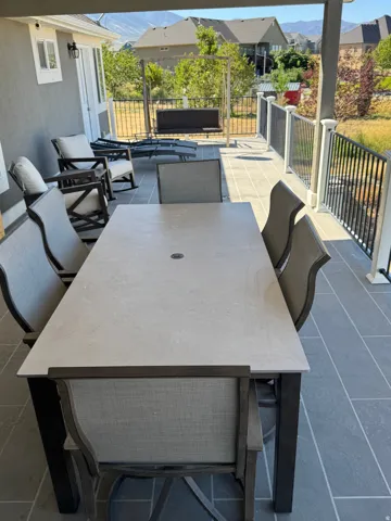 Expansive outdoor patio with dark gray tiled flooring, a white railing with black balusters, and a stucco exterior