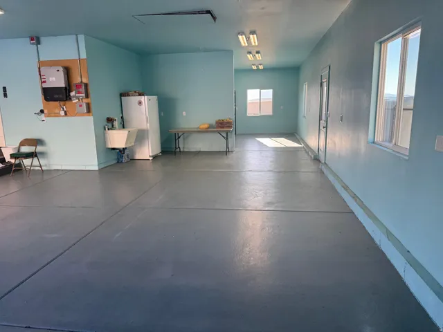 Expansive utility space with light blue walls, concrete flooring, multiple windows, built-in utility sink, and overhead lighting