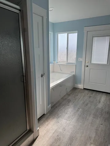 Soaking tub with a marbled surround, Vinyl flooring, and a frosted glass shower enclosure