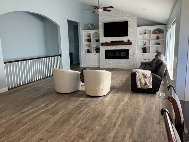 Vaulted ceiling with a ceiling fan, fireplace with a stone-finish surround, built-in shelving, Vinyl flooring, and an arched entry