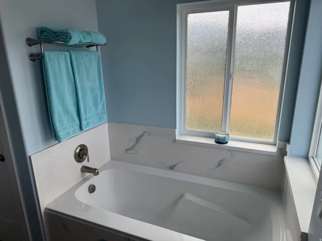Soaking tub with brushed nickel fixtures, a marbled surround, and a privacy window