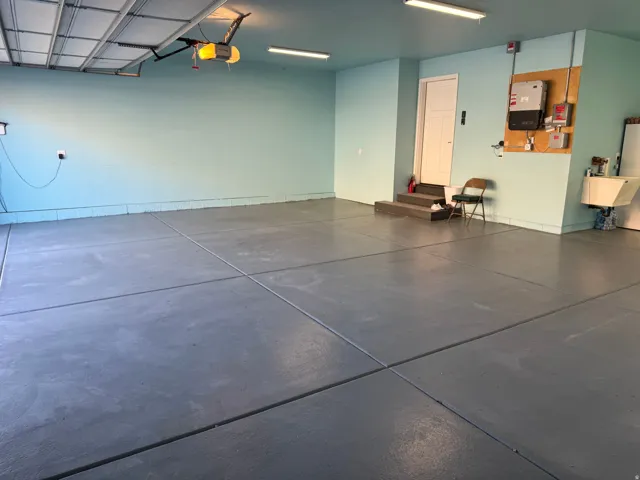 Coated concrete flooring, overhead garage door, built-in utility sink, and overhead lighting