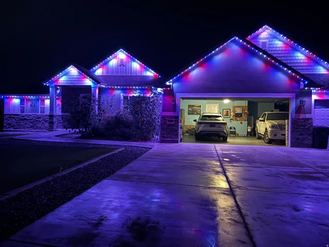 Attached two-car garage with overhead lighting, concrete driveway, and stone-clad exterior accents