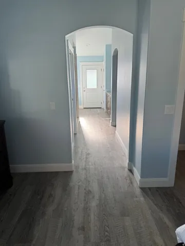 Arched entryway leading to a hallway with Vinyl flooring, light blue walls, and white trim
