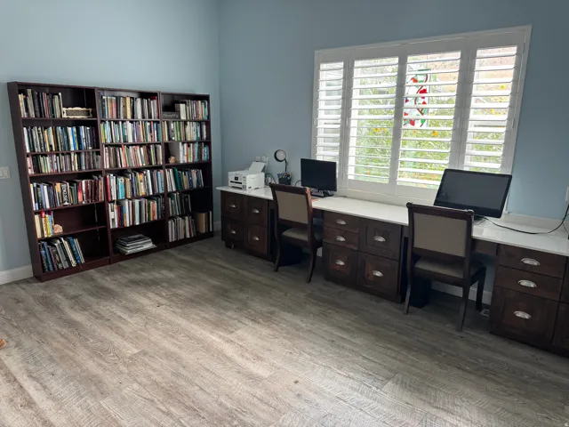 Built-in shelving, expansive window with white plantation shutters, Vinyl flooring, and a built-in desk with white countertops and dark wood cabinetry