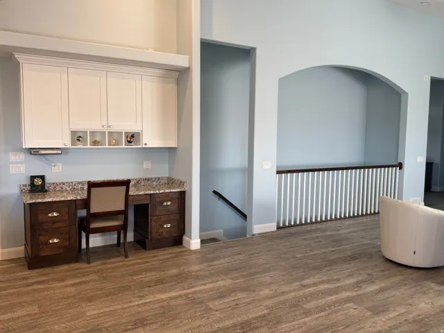 Vinyl flooring, built-in desk with stone-finish countertop, white upper cabinetry with display cubbies, and an arched architectural wall opening